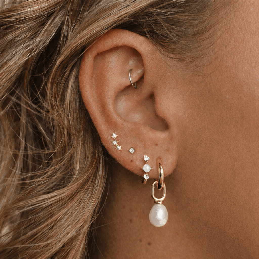 Close-up of an ear wearing multiple earrings with a pearl drop.