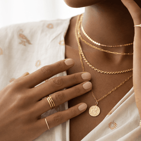 Close-up of a person wearing gold jewelry including necklaces, a ring, and a bracelet.