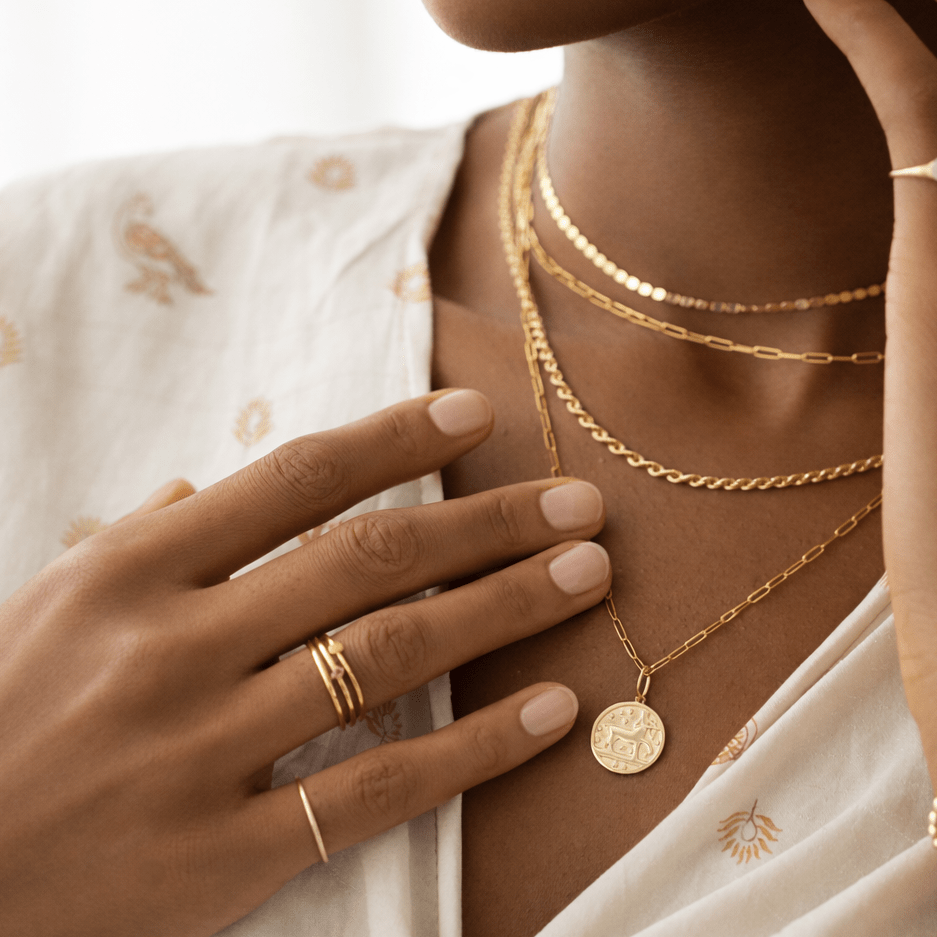 Close-up of a person wearing gold jewelry including necklaces, a ring, and a bracelet.