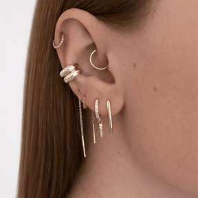 Close-up of an ear with multiple gold earrings on a plain background